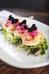 A closeup view of a plate of garnished deviled eggs, in a restaurant or kitchen setting.