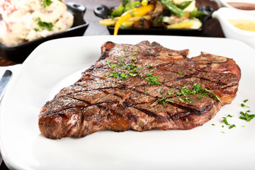 A view of a porterhouse steak dinner, with a side of mashed potatoes and vegetables.