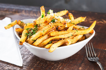 A view of a bowl of rustic garlic french fries, in a restaurant or kitchen setting.