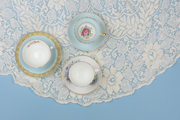 Pretty china teacups on pale blue background with white lace