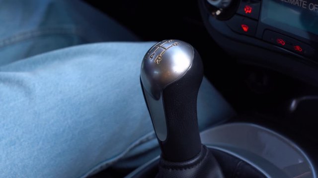 A hand of driver man in blue jacket is shifting the manual gear in a car close up. Guy controls auto and switch gears, turn on 1 gear, then 2nd, then 3rd. Male driving and changing gear 1 to 2 to 3.