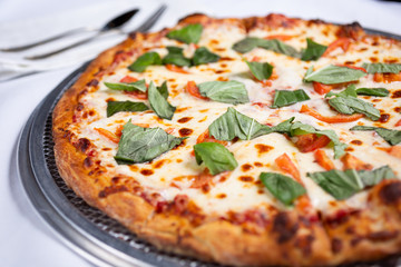 A closeup view of a Margherita pizza pie, in a restaurant or kitchen setting.