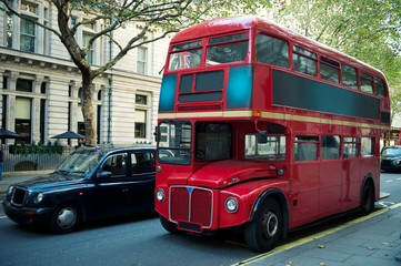 Obraz premium Traditional red double-decker Routemaster bus, introduced in 1956, making its way along an empty summer street in London, UK