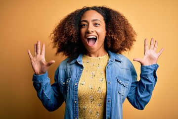 Young african american woman with afro hair wearing casual denim shirt over yellow background celebrating crazy and amazed for success with arms raised and open eyes screaming excited. Winner concept