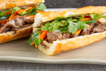 A closeup view of a teriyaki beef banh mi Vietnamese sandwich, in a restaurant or kitchen setting.