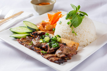 A view of a plate of grilled teriyaki chicken and rice, in a restaurant or kitchen setting.