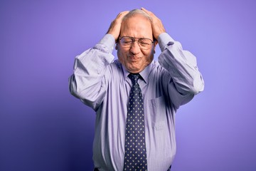 Grey haired senior business man wearing glasses standing over purple isolated background suffering from headache desperate and stressed because pain and migraine. Hands on head.