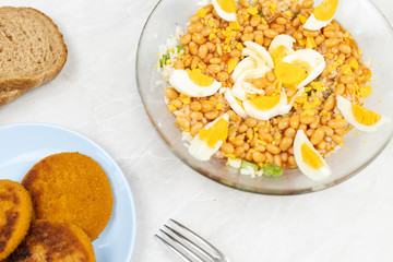 Cooked beans salad with fishcakes and bread served on the table