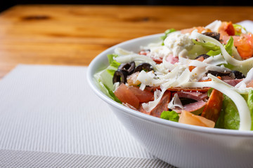 A view of a bowl of antipasto salad, cut off on the right side of the frame, in a restaurant or kitchen setting. 