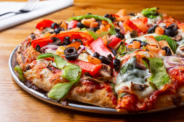 A closeup view of a personal pizza pie with meat and veggie toppings, in a restaurant or kitchen setting.