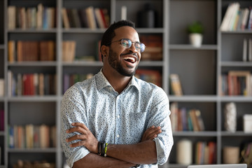 Overjoyed biracial young man in glasses stand laugh talking with friend or colleague, happy excited African American millennial male have fun engaged in pleasant conversation at home or workplace - obrazy, fototapety, plakaty