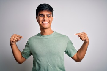 Young handsome man wearing casual t-shirt standing over isolated white background looking confident with smile on face, pointing oneself with fingers proud and happy.