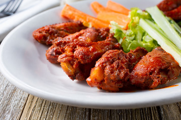 A closeup view of a plate of buffalo wings, in a restaurant or kitchen setting.