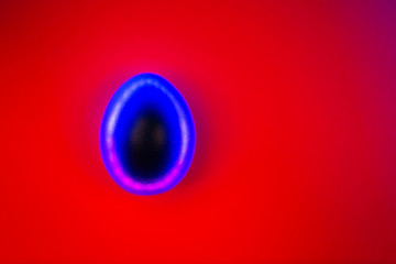 Glossy blue egg with creative neon backlight on bright red background. Easter concept. Flat lay style.
