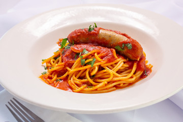 A view of a bowl of spaghetti and Italian sausage, in a restaurant or kitchen setting.