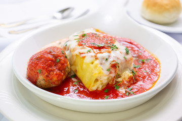 A view of a plate of lasagna and a meatball, in a restaurant or kitchen setting.