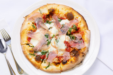 A top down view of a pizza with prosciutto toppings, in a restaurant or kitchen setting.
