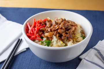 A closeup view of a Japanese rice beef bowl, in a restaurant or kitchen setting.