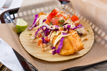 A view of a fish taco in a basket, in a restaurant or kitchen setting.