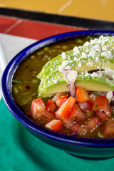 A closeup view of a bowl of pozole soup, in a restaurant or kitchen setting.