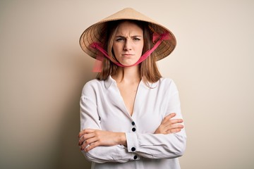 Young beautiful redhead woman wearing asian traditional conical hat over white background skeptic...