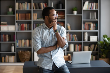 Pensive happy African American man in glasses look in distance dreaming or thinking, thoughtful...