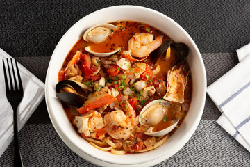 A top down view of a bowl of cioppino, in a restaurant or kitchen setting.