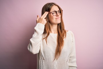 Young beautiful redhead woman wearing casual sweater and glasses over pink background Shooting and killing oneself pointing hand and fingers to head like gun, suicide gesture.