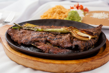 A view of a carne asada skillet plate, with a side of rice and beans, in a restaurant or kitchen...