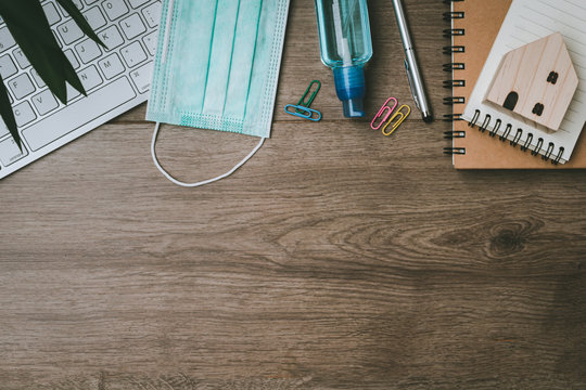 Top view of business desk at home during coronavirus and COVID-19 pandemic with blank notepad,model house, pen,hygiene face mask and Alcohol gel.Copy space. Work from home and stay at home concept
