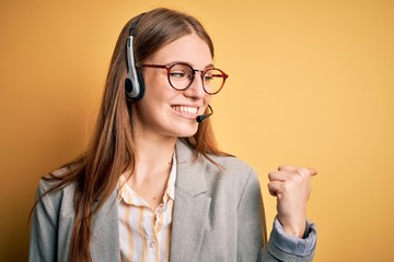 Young redhead call center agent woman overworked wearing glasses using headset smiling with happy...