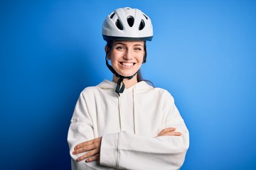 Young beautiful redhead cyclist woman wearing bike helmet over isolated blue background happy face smiling with crossed arms looking at the camera. Positive person.