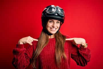 Young beautiful redhead motocyclist woman wearing moto helmet over red background looking confident with smile on face, pointing oneself with fingers proud and happy.