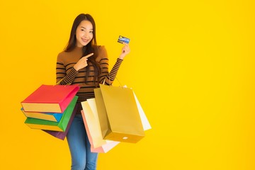 Portrait beautiful young asian woman use credit card for shopping with colorful shopping bag on yellow background