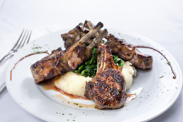 A view of a plate of lamb chops over a mound of mashed potatoes, in a restaurant or kitchen setting.