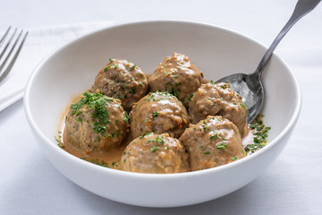 A view of a bowl of large gravy meatballs in a restaurant or kitchen setting.