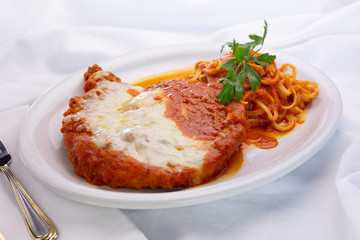 A view of a plate of parmesan chicken, in a restaurant or kitchen setting.