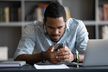 Focused African American man in glasses sit at desk check male browsing Internet on modern...