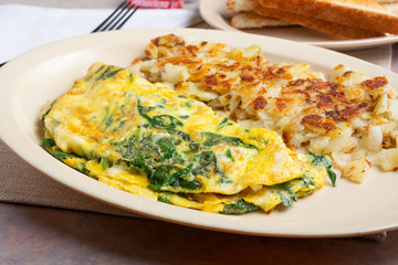 A view of a breakfast plate, featuring a spinach omelet, hash browns and a side of toast, in a restaurant or kitchen setting.
