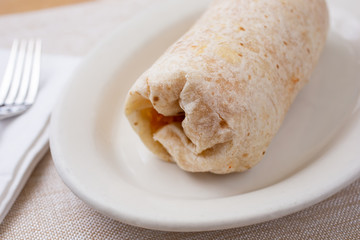 A view of a common burrito on a plate, in a restaurant or kitchen setting.