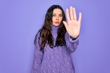 Young beautiful woman wearing casual turtleneck sweater standing over purple background doing stop...
