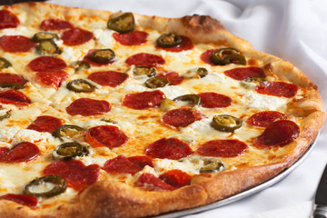 A view of a pizza pie with pepperoni and jalapeño toppings, in a restaurant or kitchen setting.