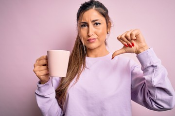 Young beautiful brunette woman drinking mug of coffee over isolated pink background with angry...