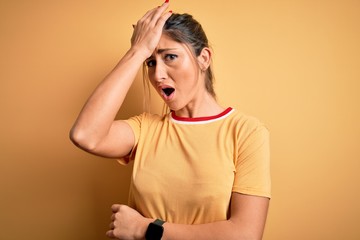 Young beautiful athletic woman wearing casual t-shirt and ponytail over yellow background surprised...