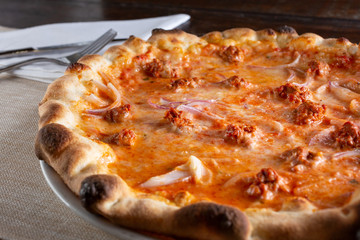 A view of a rustic pizza pie with sausage and onions, in a restaurant or kitchen setting.