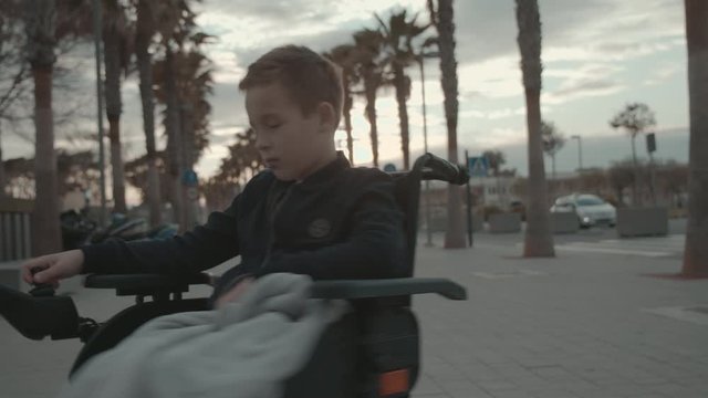 Disabled boy trying to entertain himself with spinning in electric wheelchair during evening outdoor walk