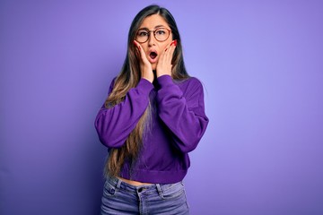 Young beautiful smart woman wearing glasses over purple isolated background afraid and shocked, surprise and amazed expression with hands on face