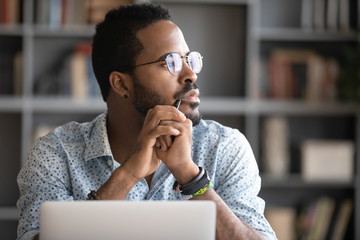 Pensive African American man in glasses distracted from computer work look in distance thinking or pondering, thoughtful biracial male lost in thoughts make plans visualizing, business vision concept - obrazy, fototapety, plakaty