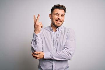 Young business man with blue eyes standing over isolated background smiling with happy face winking...