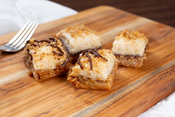 A view of pieces of baklava with chocolate syrup on a wooden board, in a restaurant or kitchen setting.